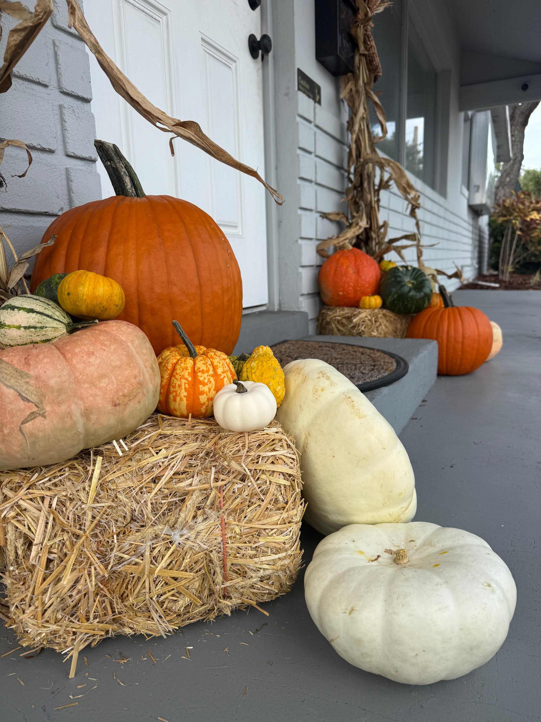 Front porch detail with pumpkin cluster on hay bale beside dried cornstalks